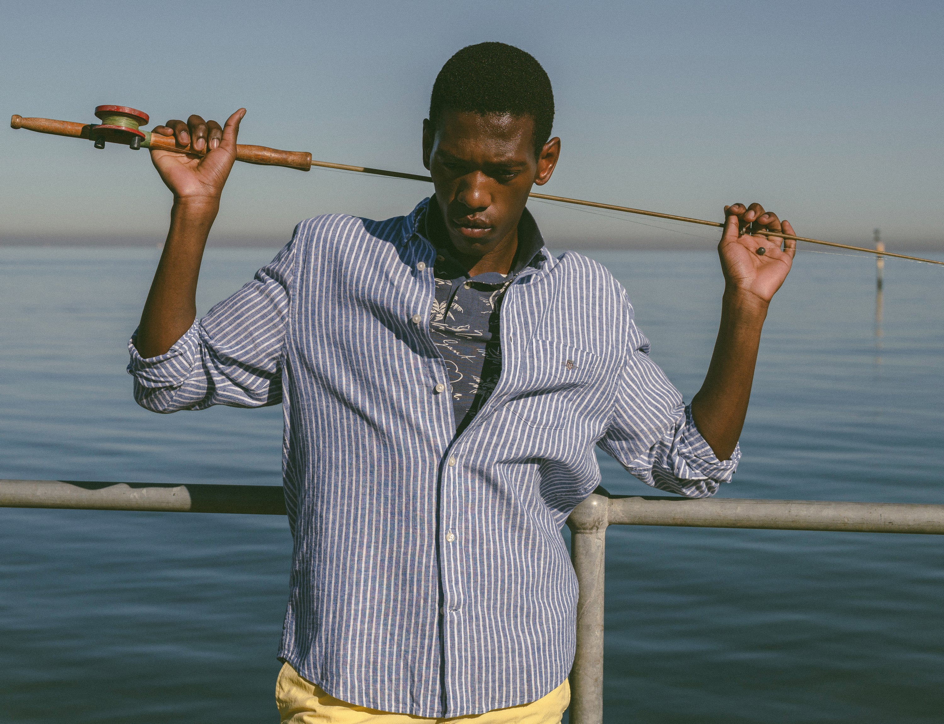 Man holding a fishing rod by a body of water in a GANT Linen Shirt.