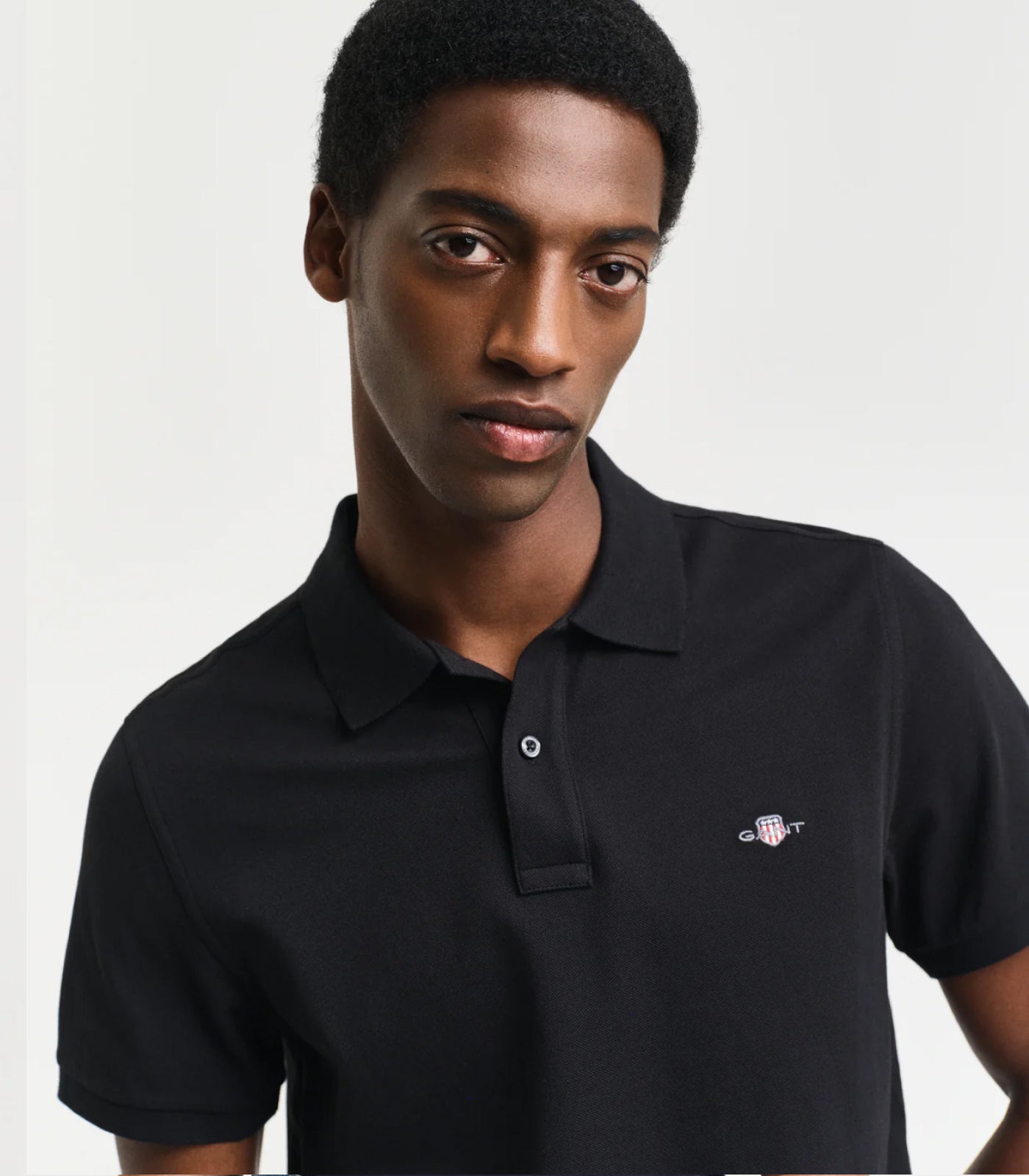 Person wearing a black GANT  polo shirt with a small logo on a light gray background