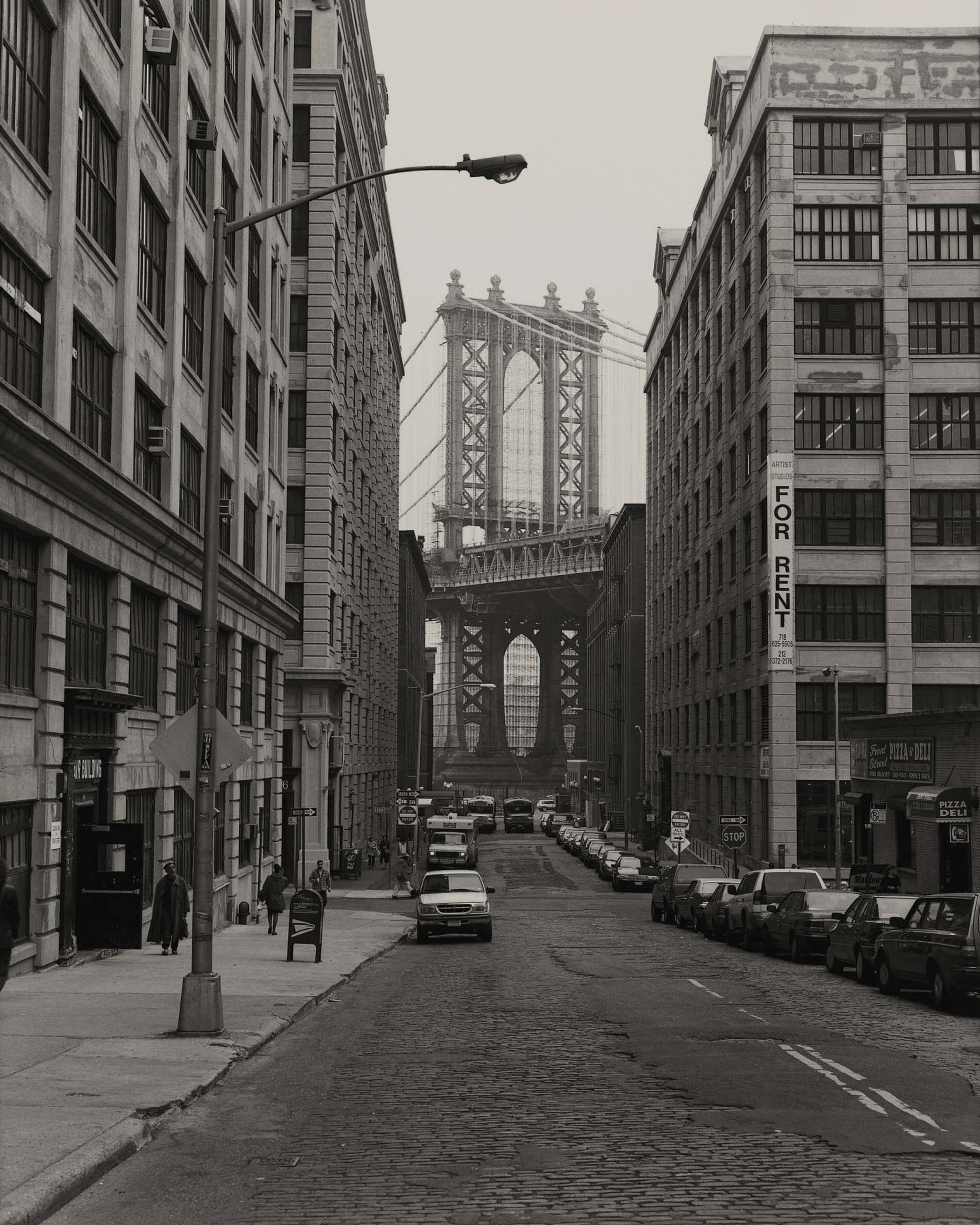 Black and white photo of a city street with the Manhattan Bridge in the background