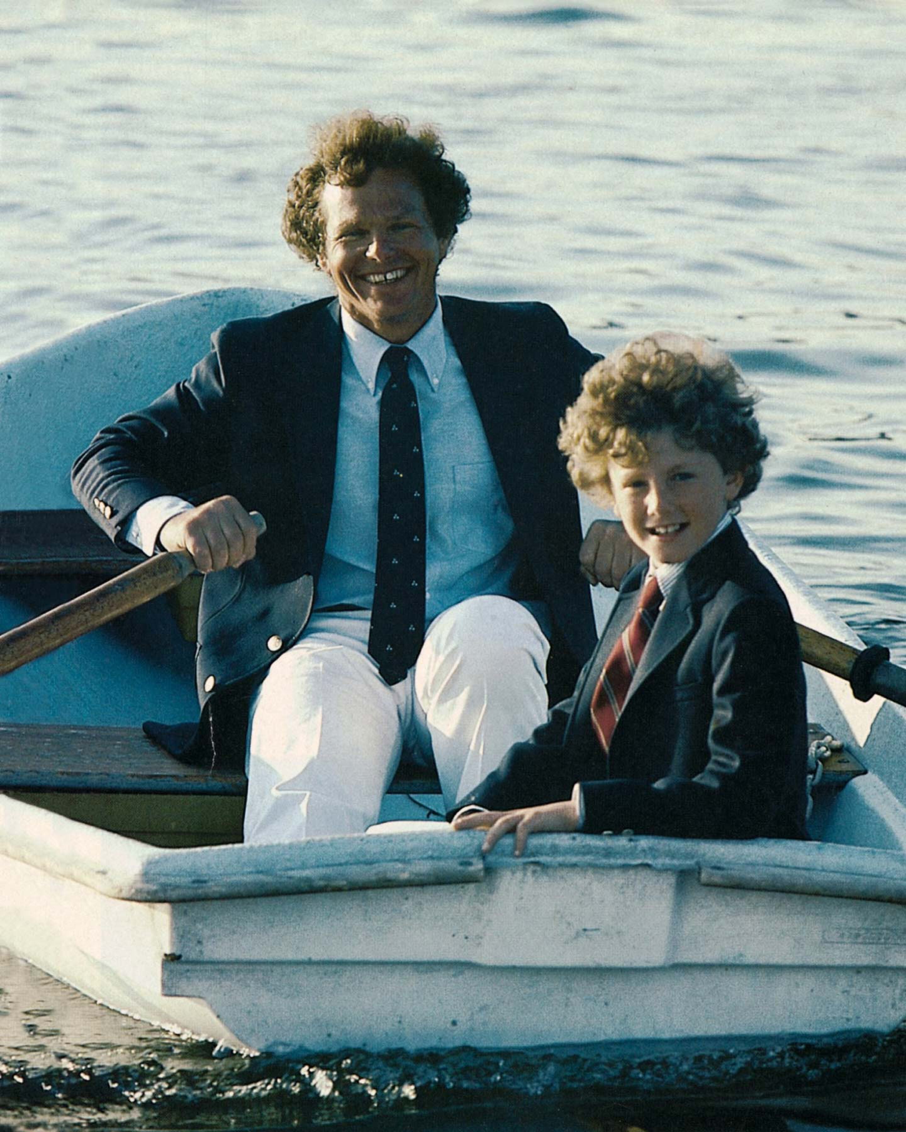 Man and child in formal attire rowing a boat on water