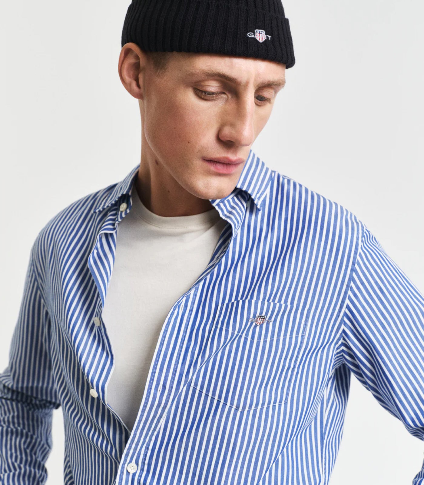 Man wearing a blue and white striped poplin shirt with a black beanie on a light gray background